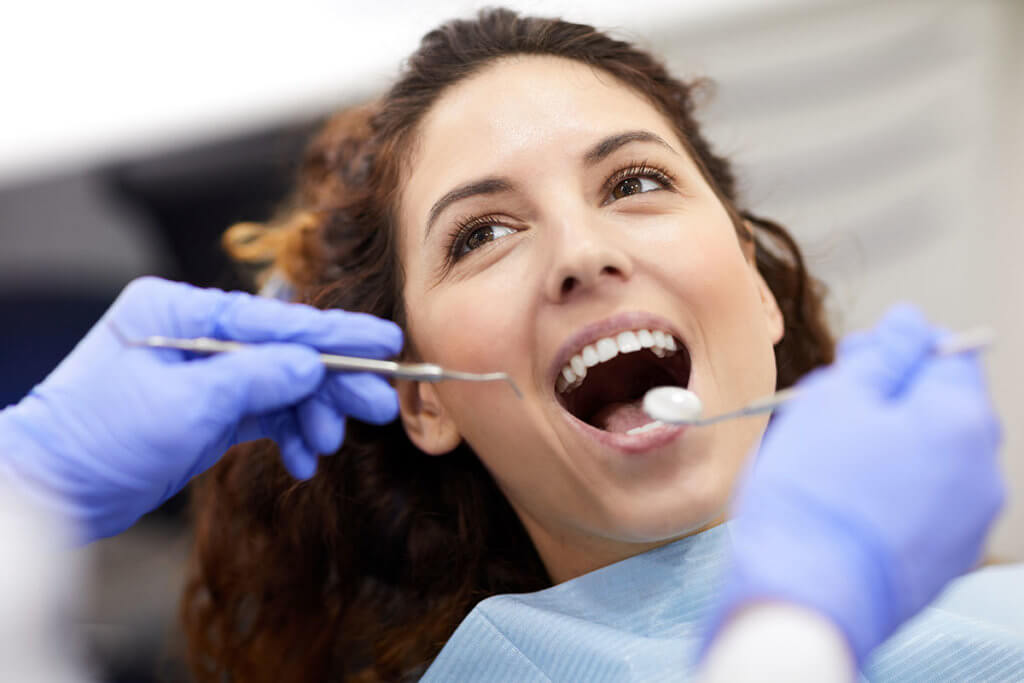 as a woman gets a check-up her dentist describes the importance of dental cleanings